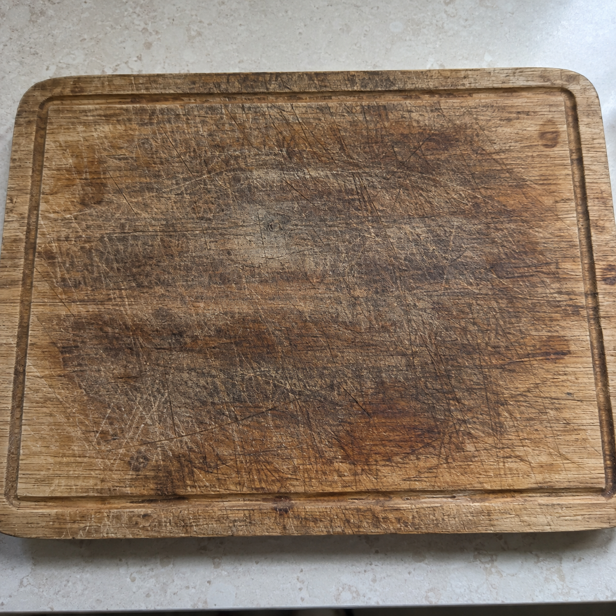 Heavily worn wooden chopping board with dark discolouration and deep knife marks